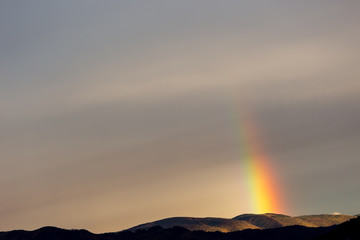 Beautiful and surreal view of part of a rainbow over some hills