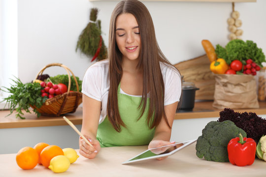 Young woman using tablet computer while cooking in kitchen. Householding, tasty food and digital technology in lifestyle concepts