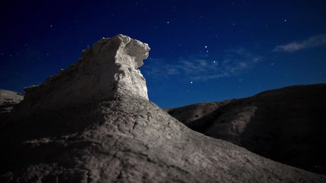 Lonely white rock on the night starry sky background in the moon looking stone canyon in Kasakhstan. Time lapse 4K shot.