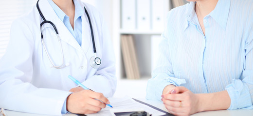 Unknown female doctor and patient discussing something while sitting at the table at hospital. Medicine and healthcare concepts
