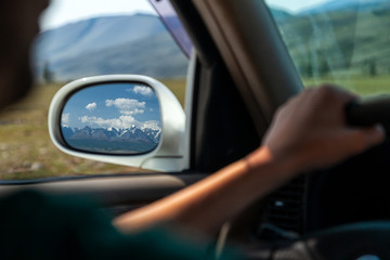 driving car on the mountain road. Guy inside the car driving on the country roadway between fields with brown grass and snowy mountains . Sun is shining. Shoot from the back.