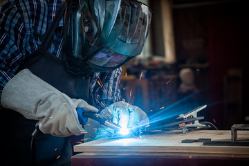 Strong man welder in work clothes hard working and welds with a welding machine metal . in the workshop