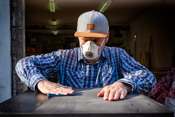 Experienced carpenter in work clothes and small business owner working in woodwork workshop,  using sandpaper for polishing wooden  at worktable in workshop