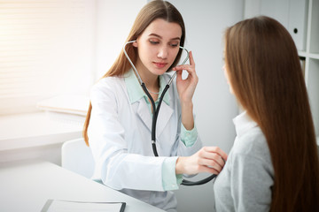 Doctor and patient in hospital. Physician examining young woman by stethoscope. Healthcare and...