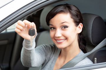 Happy owner of a new car is showing the car key. Pretty girl driver