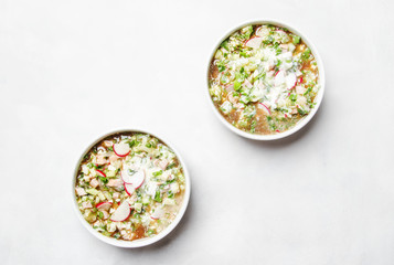 Traditional Russian summer cold soup with vegetables, herbs and meat products, white background, top view