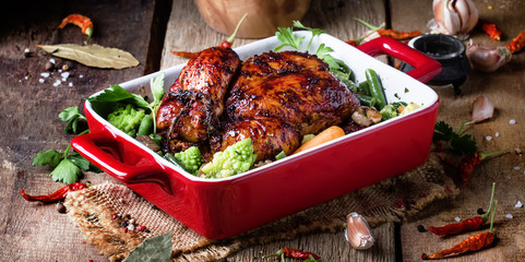Baked chicken in glaze with vegetables in red form for baking on old wooden table, rustic style,...