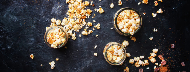 Caramel sweet popcorn in glass jars on dark background, top view