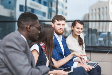 Group of happy diverse male and female business people team in formal gathered around laptop computer in bright office against the background of a glass building