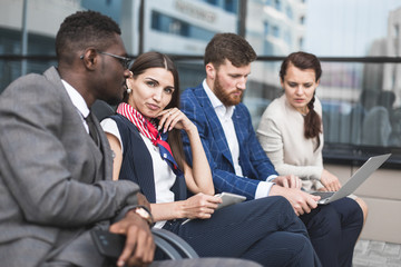 Group of happy diverse male and female business people team in formal gathered around laptop computer in bright office against the background of a glass building