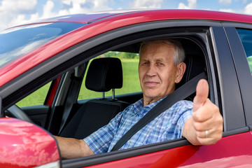 elderly man driving the car and shows the thumb