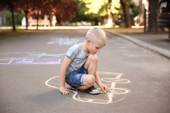 Little child drawing car with chalk on asphalt