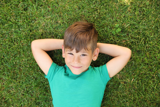 Cute little boy on green grass in park, top view. Happy child