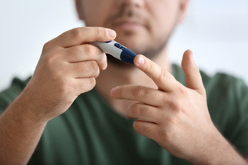 Diabetic man taking blood sample with lancet pen, closeup