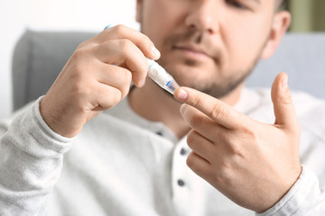 Diabetic man taking blood sample with lancet pen at home, closeup