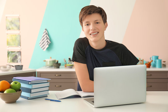 Cute Teenager Boy Using Laptop While Doing Homework In Kitchen