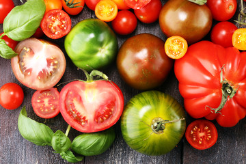 various colorful tomatoes and basil leaves on rustic table.