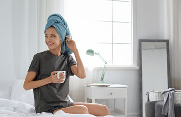 Young happy woman with cup of aromatic coffee on bed at home. Lazy morning