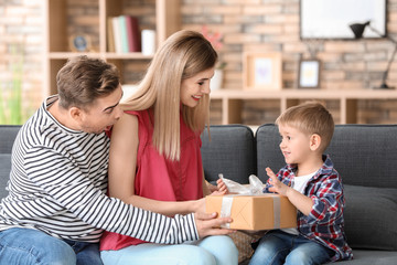 Cute little boy receiving gift from parents at home