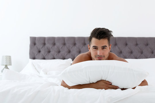 Sexy young man with soft pillow on bed at home