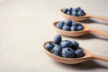Wooden spoons and juicy blueberries on color table