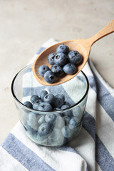 Spoon with juicy and fresh blueberries over glass on color table