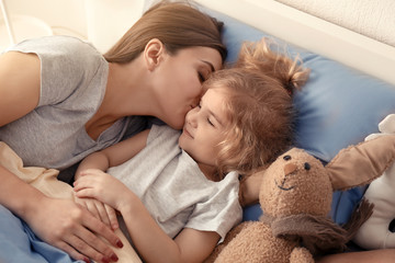 Mother kissing her sleeping daughter in bed at home. Family bedtime