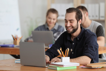 Obraz premium Male student with laptop doing homework in classroom
