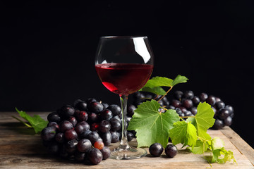 Fresh ripe juicy grapes and glass of red wine on table against black background