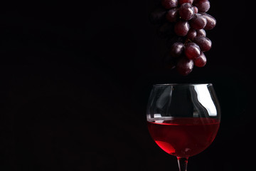 Fresh ripe juicy grapes over glass with red wine and space for text on black background