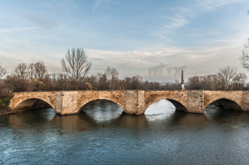 Steinbrücke an Fluss vor Dampfwolken eines Kohlekraftwerkes