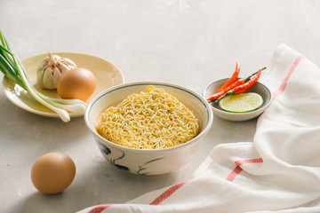 Instant noodles in bowl and vegetable side dishes on stone background. Quick & easy food concept.