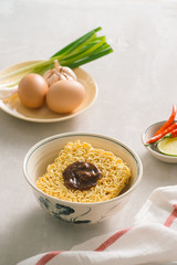 Instant noodles in bowl and vegetable side dishes on stone background. Quick & easy food concept.