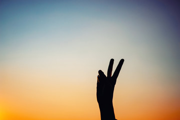 Female hand shows silhouette sign of victory or peace at sunset, copy space