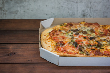 Pizza on wooden background in rustic style. Italian pizza from the shop in a cardboard box. Simple food on a wooden background. Tasty dish for lunch