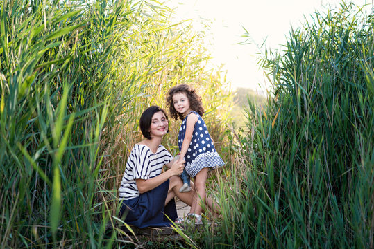 Beautiful and lovely mother with a little daughter secrets in the reeds on the lake