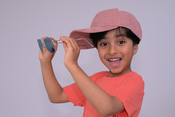 Cheerful child wearing pink hat holding sunglasses. Happy little kid ready to wear sunglasses looking at camera. 