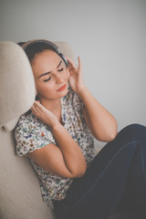 Pretty, young woman listening to her favorite music on hi-fi headphones sitting in a designer chair