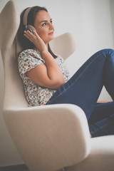 Pretty, young woman listening to her favorite music on hi-fi headphones sitting in a designer chair