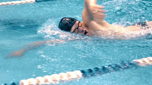 Medium close up torso of athletic young swimmer performing crawl style in swimming pool