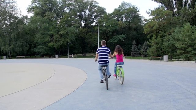 HD A Couple riding bicycles in the park, on block stones View from back
