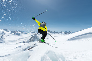 A skier in full sports equipment jumps into the abyss from the top of the glacier against the background of the blue sky and the Caucasian snow-capped mountains. View from the back. Elbrus region