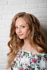 Portrait of a brown-haired woman with clean skin and long hair against a white brick wall close-up.