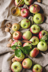 Ripe organic gardening green red apples with leaves, walnuts, cinnamon and jar of honey over linen cloth as background. Flat lay, space. Autumn harvest.
