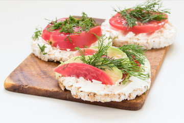 Fototapeta na wymiar round crisp breads with cheese, tomatoes and avocado on a cutting board