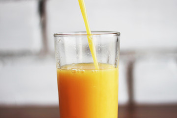 freshly squeezed orange juice pours into glass on brick wall background in loft style