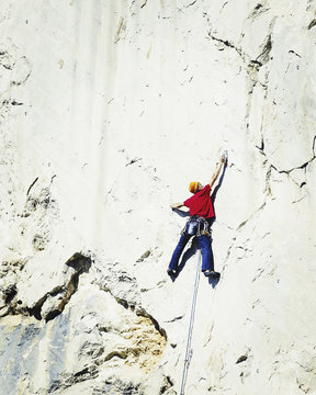 Young man looking up while climbing challenging route on cliff.