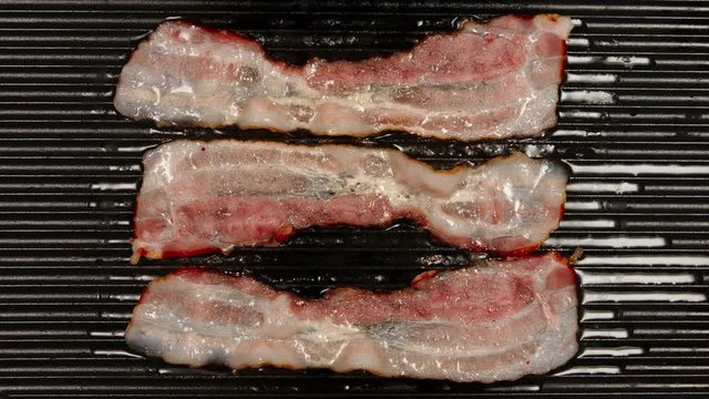 TOP VIEW: Frying a strips af bacon on a black pan