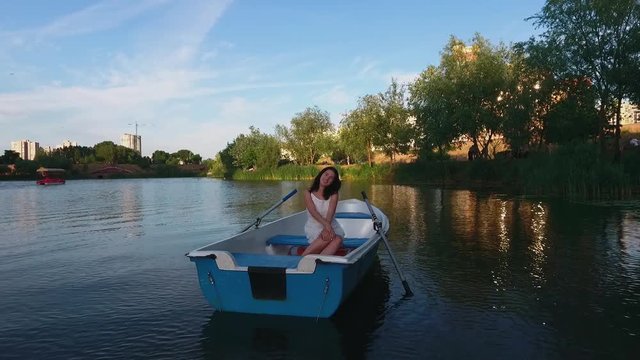 Beautiful girl is sitting in a boat on the lake and waving her arms