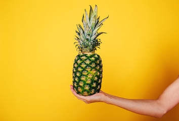 Female hand holding ripe pineapple on a orange background, Nutrition concept